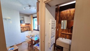 A compact kitchen with white cabinets, a dining area with a table and chairs, and a bathroom with a sink and mirror.
