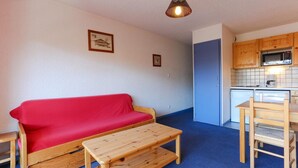 A compact living space with a red sofa, wooden coffee table, and a kitchenette area with wooden cabinets and a microwave. - Alpine Retreat with Balcony (Les Deux Alpes)