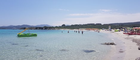 A beach with clear water, people, and a green inflatable boat.