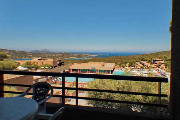 Un balcón con vista a la costa, que incluye edificios y una piscina.