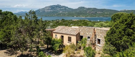 Un edificio de piedra con techo de tejas, rodeado de pinos y vistas a un lago y montañas.