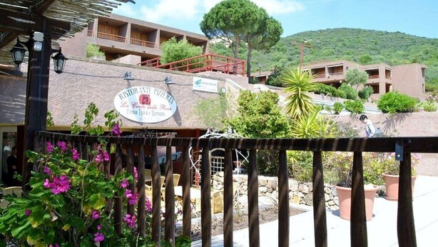 Un restaurante con terraza, fachada de piedra y vistas a una colina.