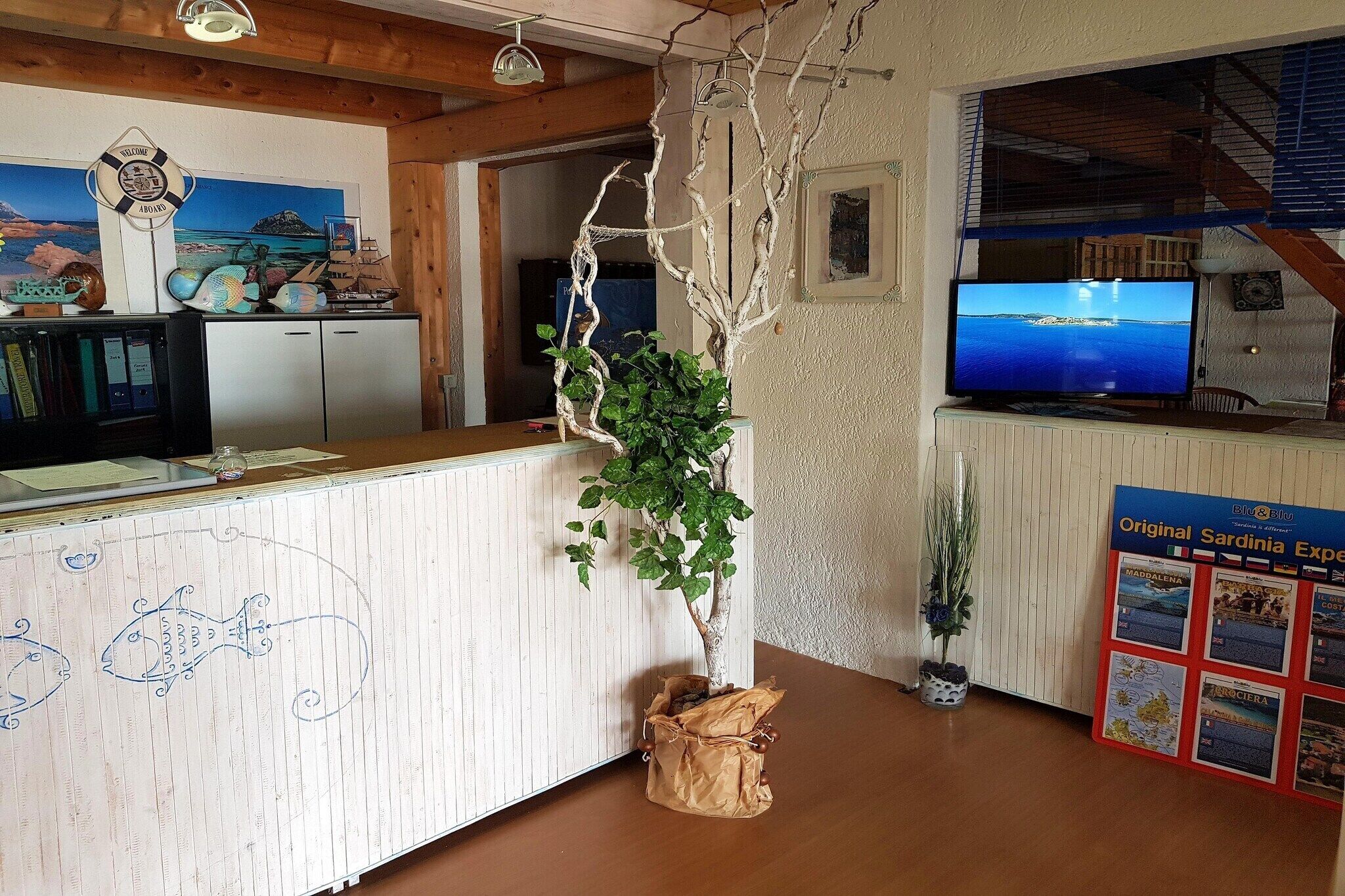 Ein Empfangsbereich mit einem Holzbüro, einem an der Wand befestigten Fernseher und einem Schwarzesbrett mit Reiseinformationen.