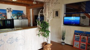 Un área de recepción con un mostrador de madera, un televisor montado en la pared y un tablón de anuncios con información turística.