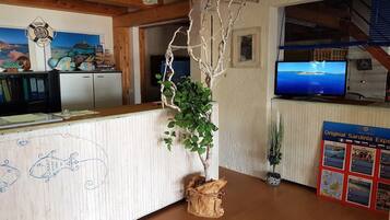 Ein Empfangsbereich mit einem Holzbüro, einem an der Wand befestigten Fernseher und einem Schwarzesbrett mit Reiseinformationen.