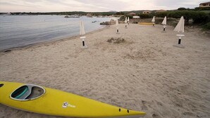 Una playa con un kayak amarillo, sombrillas blancas y un mar tranquilo.