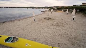 Ein Strand mit einem gelben Kajak, weißen Sonnenschirmen und ruhiger See.