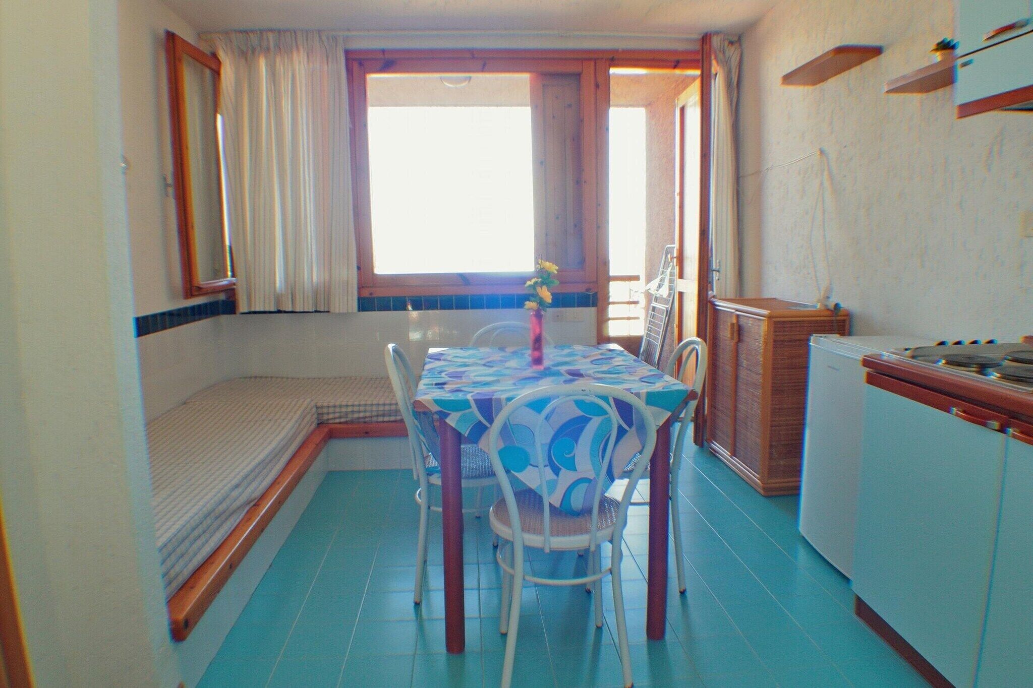 Habitación compacta con mesa de comedor, sillas, una pequeña kitchenette y una ventana con cortinas.