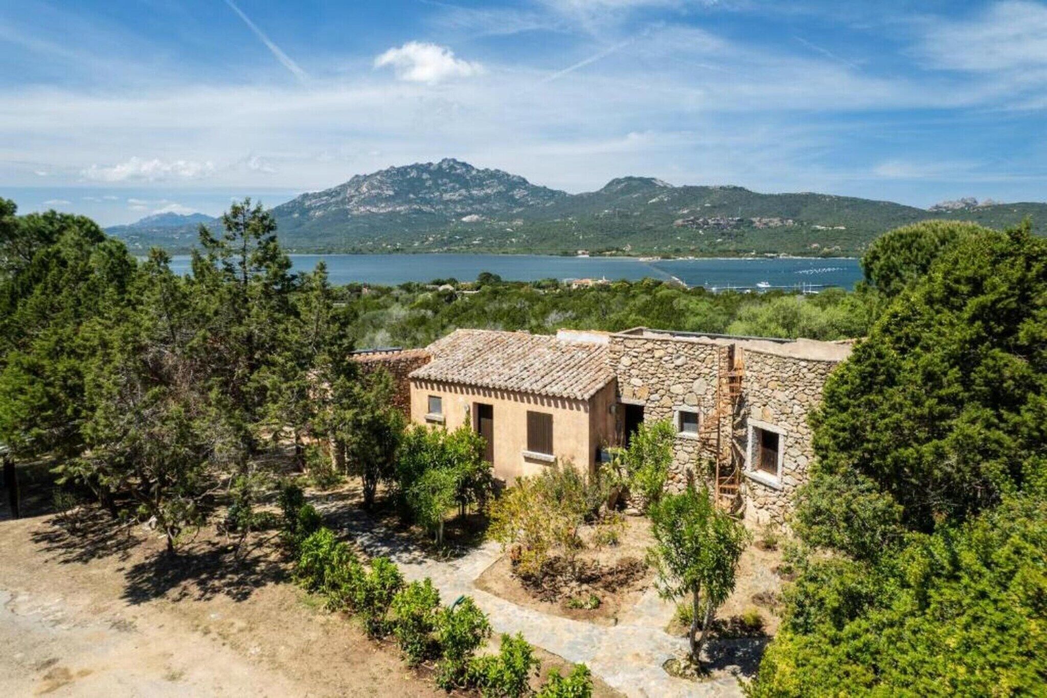 Un bâtiment en pierre avec un toit en tuiles, entouré d’arbres et offrant une vue sur un lac et des montagnes.