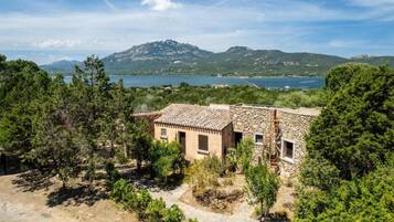 Un bâtiment en pierre avec un toit en tuiles, entouré d’arbres et offrant une vue sur un lac et des montagnes.