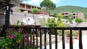 Ein Restaurant mit Terrassensitzgelegenheiten, einer steinernen Fassade und Blick auf einen Hügel.