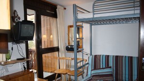 Ein Schlafsaal mit Etagenbetten, einem Fernseher, Holzstühlen, einem gestreiften Sofa und einem kleinen Tisch.