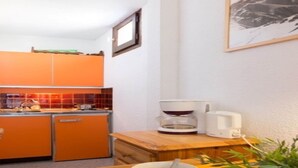 Eine kompakte Küche mit orangefarbenen Schränken, einer Kaffeemaschine und einem kleinen Esstisch mit Schüssel und Weinglas.