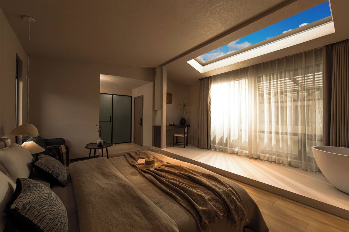 Ett modernt hotellrum med en stor säng, ett takfönster, en matplats och utsikt över himlen.