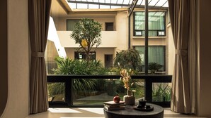 Ein modernes Interieur mit einem Balkon, der auf einen Garten und ein Gebäude blickt. Es steht ein runder Tisch mit Büchern und einer Vase darauf.