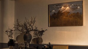 Ein Essbereich mit einem Tisch für zwei Personen, einer Vase mit Zweigen und einem Gemälde von Bergen und Vögeln an der Wand.