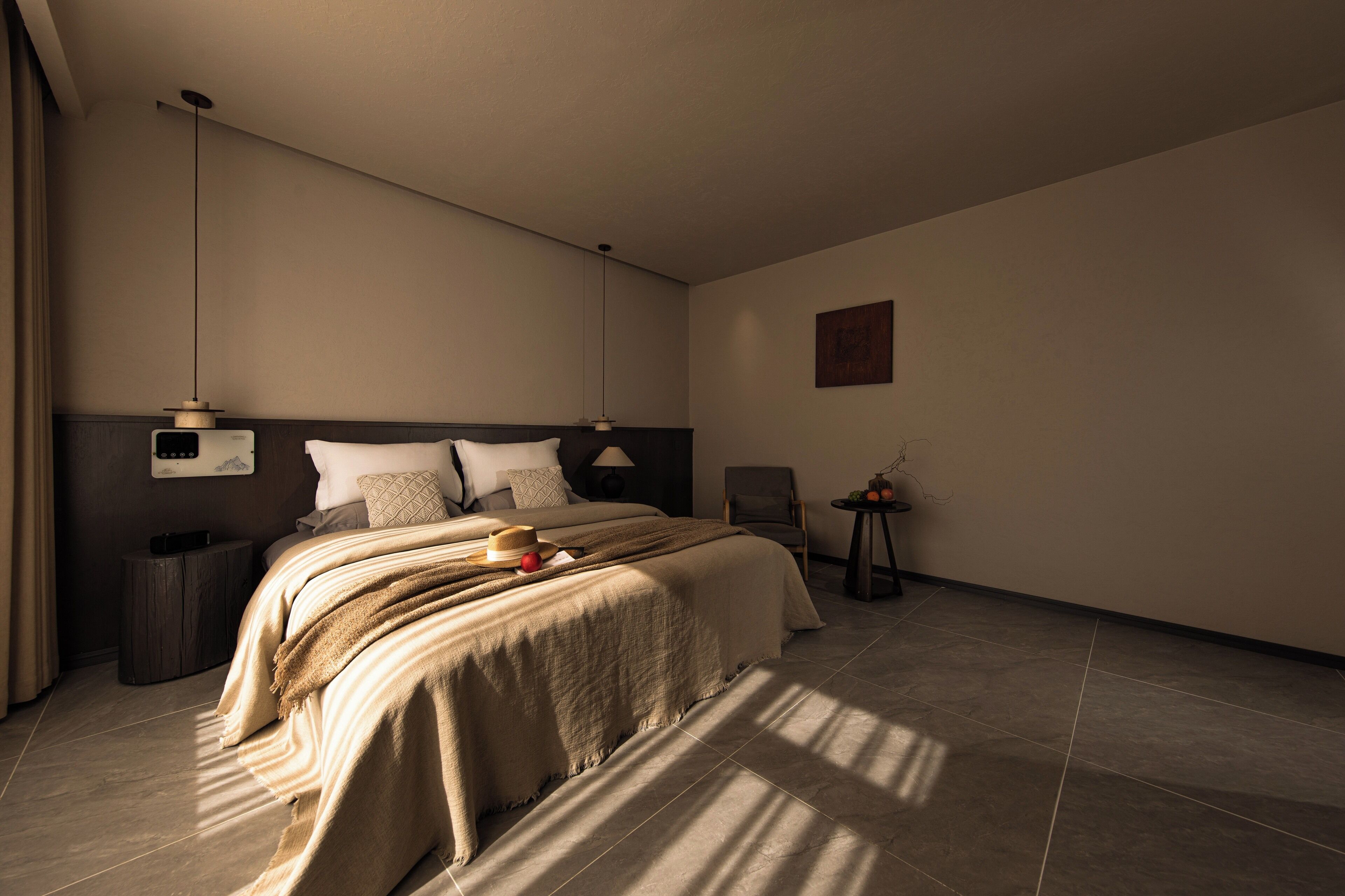 A modern hotel room with a large bed, a bedside table, a chair, and a small table with a vase.