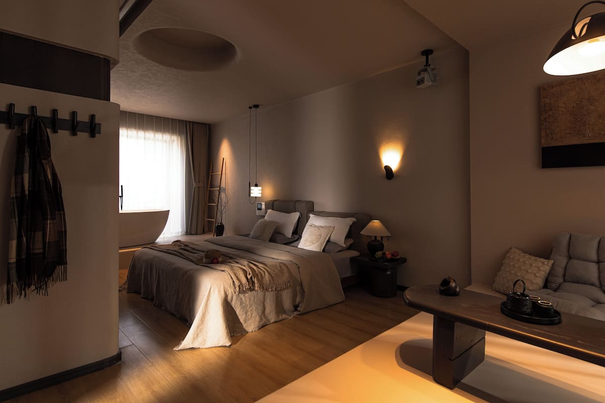 Une chambre moderne avec un grand lit, des tables de chevet, un banc et un luminaire fixé au mur.