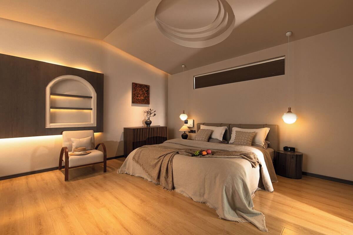 Une chambre moderne avec un plancher en bois, un grand lit avec une tête de lit, des tables de chevet, une chaise et une étagère fixée au mur.
