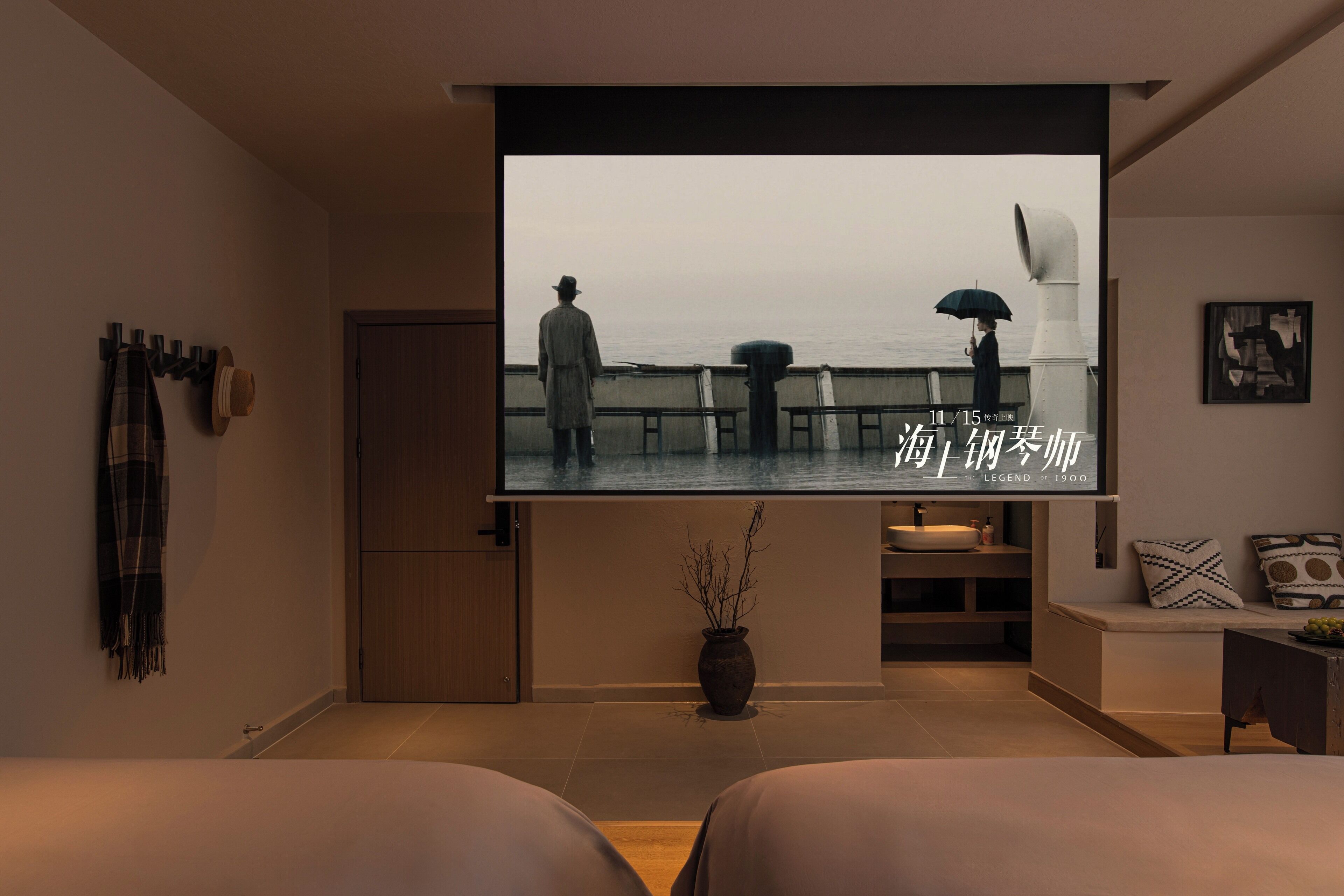 A modern hotel room with a large TV screen displaying a scenic view, a cozy seating area with a bench, and a minimalist decor style.