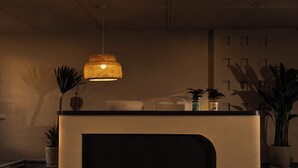 Ein Empfangstresen mit einer gewebten Pendelleuchte, Topfpflanzen und einem an der Wand befestigten Schild.