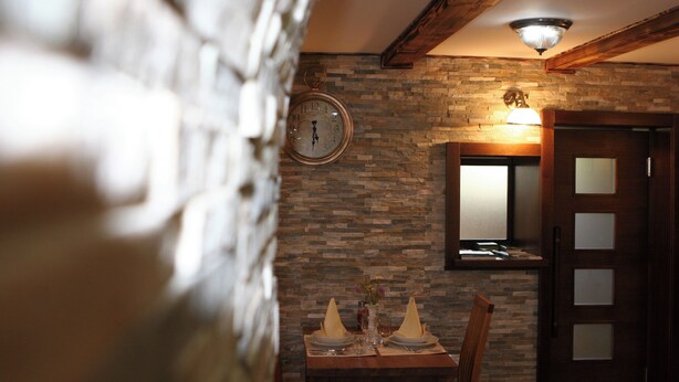 A dining area with a stone wall, a wooden ceiling, and a clock. - Millenium House (Plitvicka Jezera)