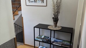 A hallway with a black console table displaying magazines, a framed picture on the wall, and a staircase in the background. - Millenium House (Plitvicka Jezera)