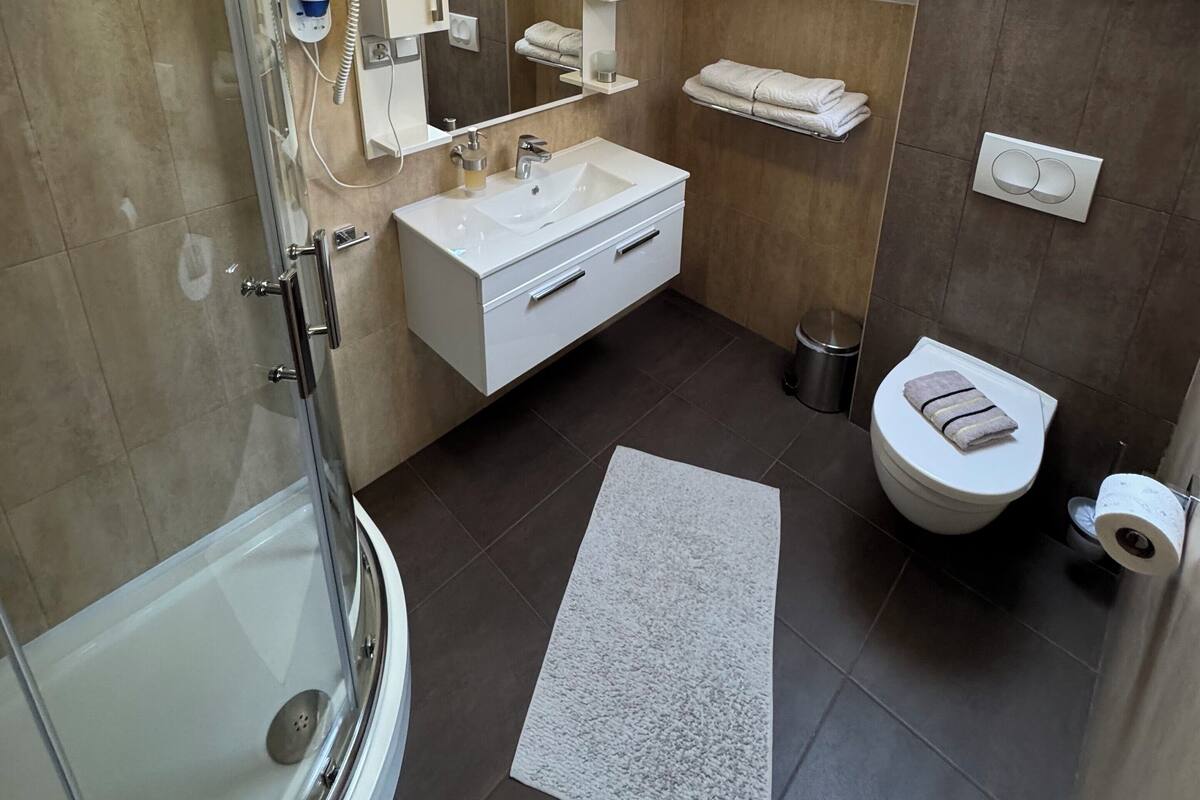 A modern bathroom with a glass-enclosed shower, a white vanity with a mirror, a towel rack, and a skylight.