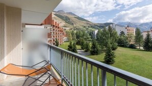 A balcony with a view of a mountainous landscape, a grassy area, and a building with a red facade.