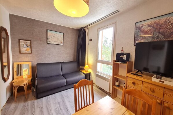 A modern living room with a sofa, a wooden dining table, and a TV. - Cozy Mountain Base Near Slopes (Les Deux Alpes)