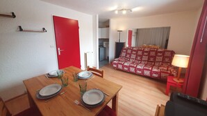 Un coin repas avec une table en bois dressée pour quatre personnes, une porte rouge et un canapé à motifs en arrière-plan.