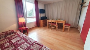 Une chambre à coucher avec un lit, un bureau, une chaise, un téléviseur et une fenêtre avec des rideaux.