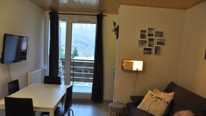 Ett rum med ett matbord, stolar, en soffa, en liten pall och en tv som är monterad på väggen.