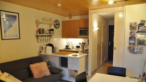 Ett kompakt bostadsutrymme med ett litet kök, en soffa, ett matbord och ett kylskåp.
