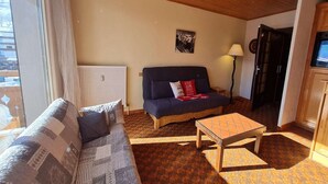 A cozy living room with a sofa, a small table, a radiator, and a lamp. - Ski-In Apartment with Balcony (Les Deux Alpes)