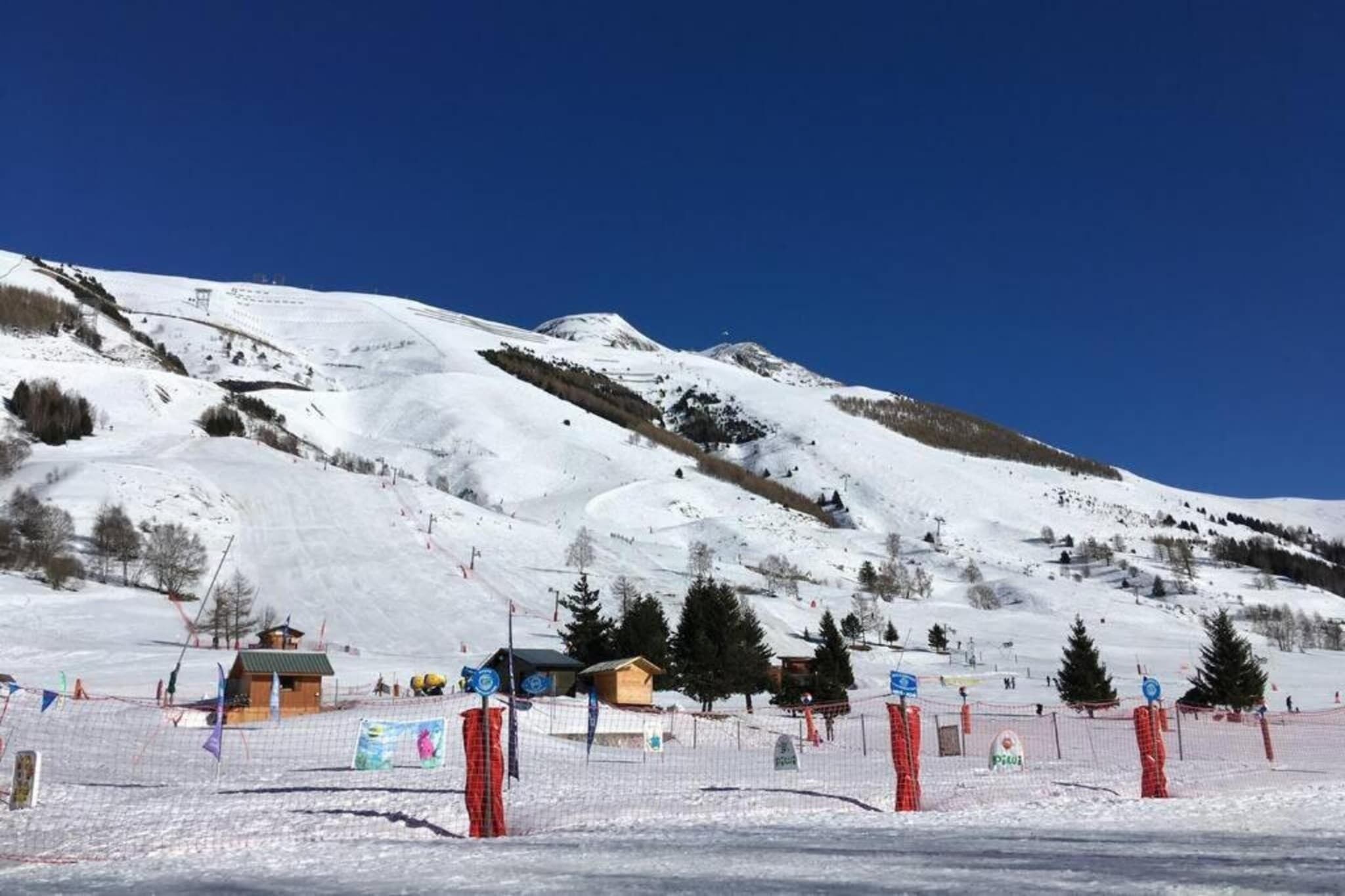Une piste de ski enneigée, avec un chalet en bois et une zone délimitée par une clôture.
