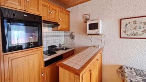 A compact kitchen with wooden cabinets, a black oven, a microwave, and a tiled backsplash. - Ski-In Apartment with Balcony (Les Deux Alpes)