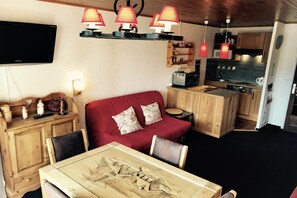 Uma sala de estar acolhedora com um sofá vermelho, armários de madeira, uma mesa de jantar com design exclusivo e uma cozinha com armários de madeira e micro-ondas.