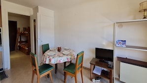 A compact room with a dining table set for four, a television on a stand, and a bookshelf. - Ski on rue du Grand Plan (Les Deux Alpes)
