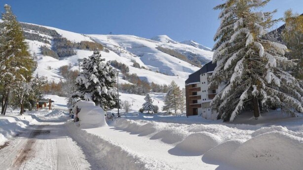 Una carretera nevada que conduce a un edificio, con un telesilla de esquí al fondo.