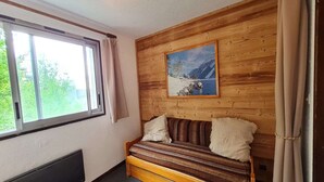Una habitación acogedora con pared de madera, una ventana con cortinas, un sofá con cojines y un cuadro de un paisaje nevado.