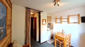 Una habitación compacta con una mesa de comedor de madera, una pequeña kitchenette y una puerta que da a otra habitación.