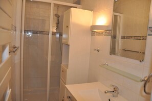 Bathroom features a walk-in shower with a glass door, a white cabinet for storage, and a glass shelf above the sink.