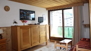 Ein Zimmer mit Holzbalkendecke, einem Holzschrank, einem Fernseher, einem kleinen Tisch, einem Bett und einem Fenster mit Blick auf Gebäude.
