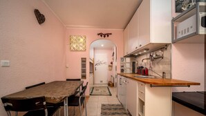 A compact kitchen with a dining area, featuring a wooden table and chairs, a small countertop, and a white cabinet. - Studio in France with Mountain Views (Allos)