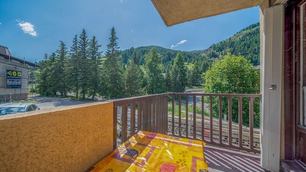 A balcony with a view of a forested mountain and a building with a sign. - Studio in France with Mountain Views (Allos)