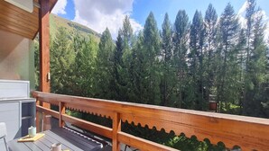Terraza de madera con mesa y sillas, con vistas a una ladera boscosa.