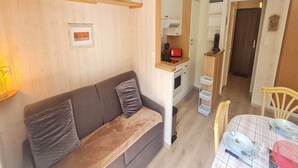 Una sala de estar acogedora con un sofá, una mesa de comedor dispuesta con platos y cubiertos, y una cocina visible al fondo.