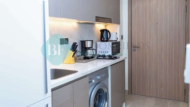 A modern kitchen with a dishwasher, coffee maker, and a wooden door. - Bloomfields Mesmerizing STU Azizi Rivera (Dubai)