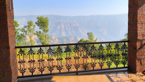 A balcony with a wrought iron railing, a brick wall, and a view of a canyon landscape. - Eagle Eye Resort (Mahabaleshwar)